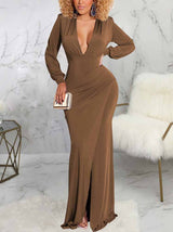 Woman wearing a long brown dress with a deep V-neckline, long sleeves, ruched detailing, and a high slit.
