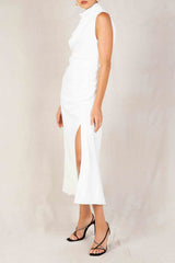 Side view of a woman in a white satin halter neck midi dress with a draped bodice and a thigh-high slit.