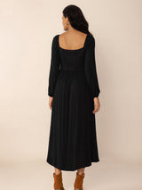 Back view of a woman wearing a black midi dress with a square neckline, long puff sleeves, and a corset-style waist detail.