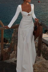 Woman in a white long sleeve maxi dress with a cutout and sweetheart neckline, holding a brown handbag.