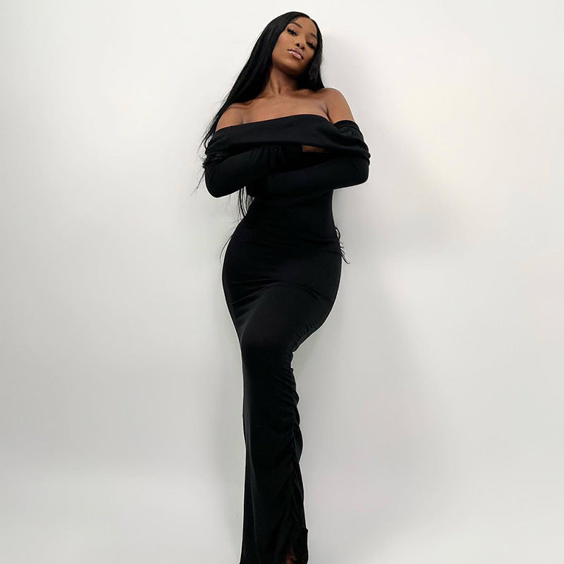 Woman wearing a long black off-the-shoulder dress with long sleeves, standing with arms crossed against a white background.