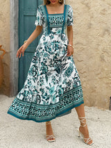 Woman wearing a white midi dress with a green floral print and short puff sleeves, standing outdoors.