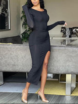 A woman poses in a black long-sleeved midi dress with a prominent side slit, highlighting the fabric's texture and the dress's form-fitting style.