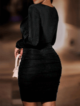 Back view of a woman in a black ruched bodycon dress with a halter neckline and long sleeves.