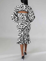 Rear view of a woman wearing a black and white leopard print knit dress with a high neck, cut-out detail, long puff sleeves, and a mermaid hemline.