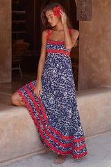 Woman wearing a blue and white animal print maxi dress with red scalloped trim and red flower in her hair, posing outdoors.
