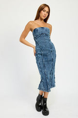 Woman wearing a blue strapless denim midi dress with paneled construction and raw edge detailing, standing against a white backdrop.