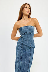 Woman wearing a blue strapless denim midi dress with paneled construction and raw edge detailing, posing with hands on hips.