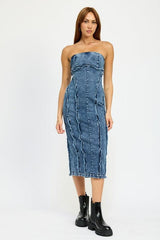 Full body shot of a woman in a blue strapless denim midi dress with paneled construction and raw edge detailing, paired with black boots.