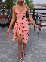 Woman wearing a pink sleeveless dress with black hearts and a high slit.
