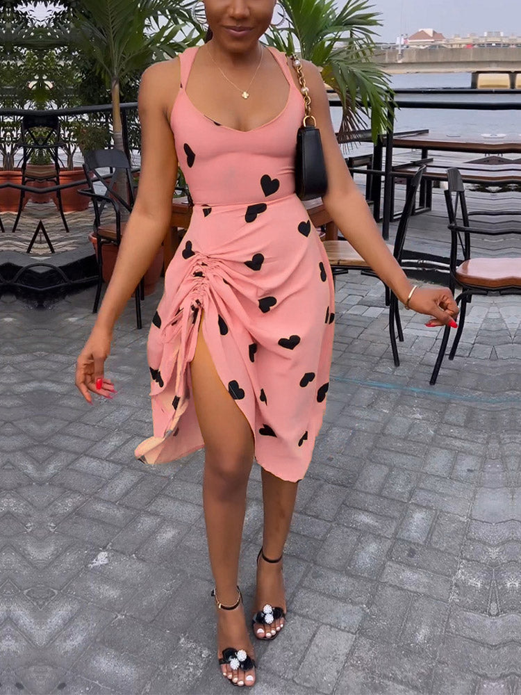 Woman wearing a pink sleeveless dress with black hearts and a high slit.