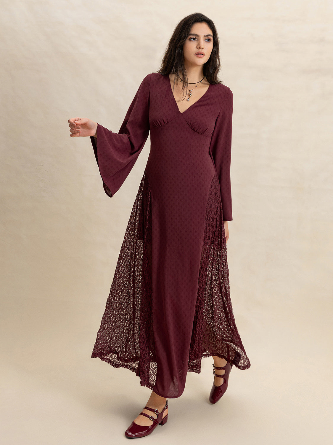 Full-body shot of a woman in a burgundy maxi dress with flared sleeves and intricate lace detailing on the skirt.