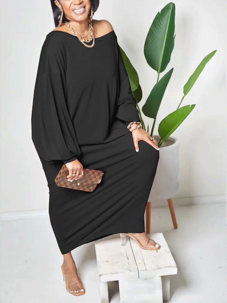 Woman in a black off-the-shoulder maxi dress with balloon sleeves, sitting on a stool, holding a checkered clutch.