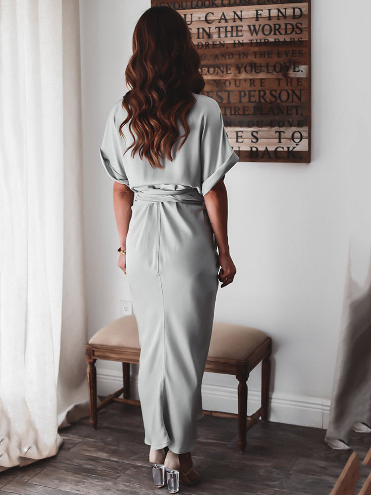 Back view of a woman wearing a light gray satin maxi dress with short sleeves and a tie waist.
