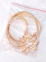 Close-up of a gold elastic belt with a floral embellishment and rhinestones, packaged in plastic.