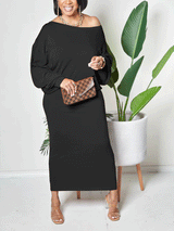 Woman wearing a black off-the-shoulder maxi dress with balloon sleeves and clear heels, holding a checkered clutch, standing next to a potted plant.
