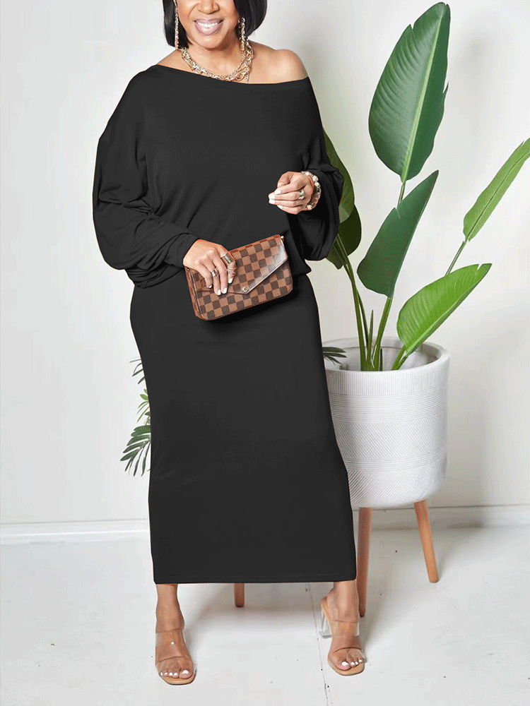 Woman wearing a black off-the-shoulder maxi dress with balloon sleeves and clear heels, holding a checkered clutch, standing next to a potted plant.