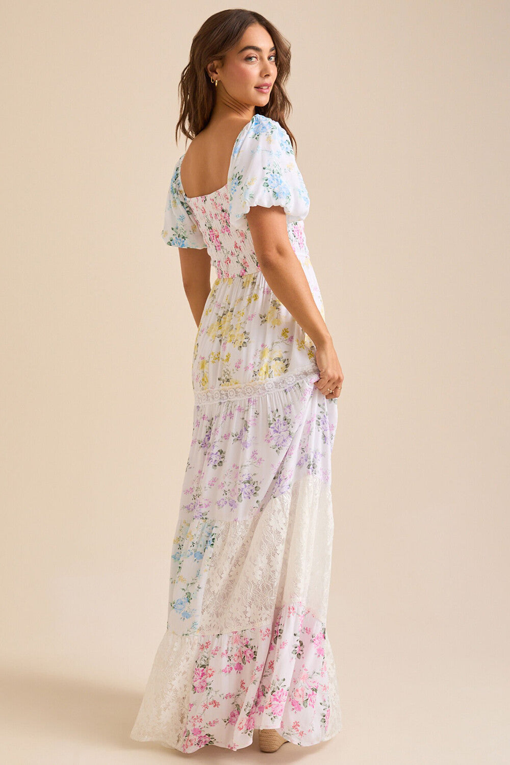 Back view of a woman wearing a white floral print maxi dress with puff sleeves and a square neckline.