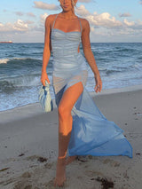 Woman wearing a light blue ruched mesh maxi dress with a high slit and spaghetti straps on a beach.