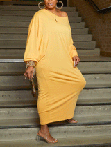 Front view of a woman in a yellow off-the-shoulder maxi dress with balloon sleeves, holding a checkered clutch.