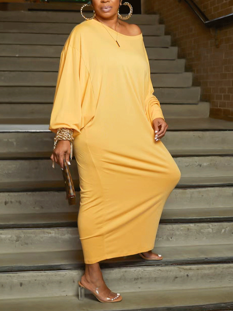 Front view of a woman in a yellow off-the-shoulder maxi dress with balloon sleeves, holding a checkered clutch.