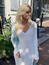 Woman with blonde hair wearing a white ribbed knit maxi dress with flared cuffs, carrying a light blue handbag.