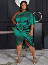 Woman wearing a green one-shoulder satin dress with draping and a tulip hem, posing with hand on hip.