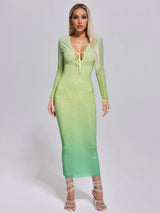 Woman wearing a long, form-fitting, gradient green dress with long sleeves and a plunging neckline adorned with rhinestones.