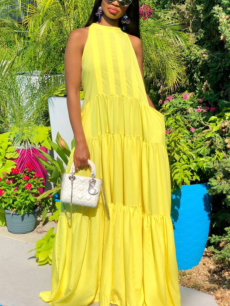 Full shot of a woman wearing a yellow tiered maxi dress with a halter neckline.