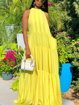 Full shot of a woman wearing a yellow tiered maxi dress with a halter neckline.