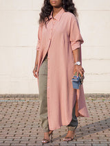 Woman wearing a long pink collared shirt dress over olive green cargo pants and heels, holding a blue and green clutch.