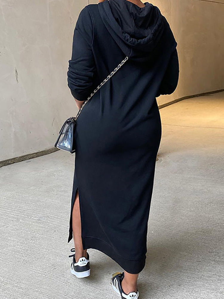 Rear view of a woman in a long black hooded dress with side slits and sneakers.