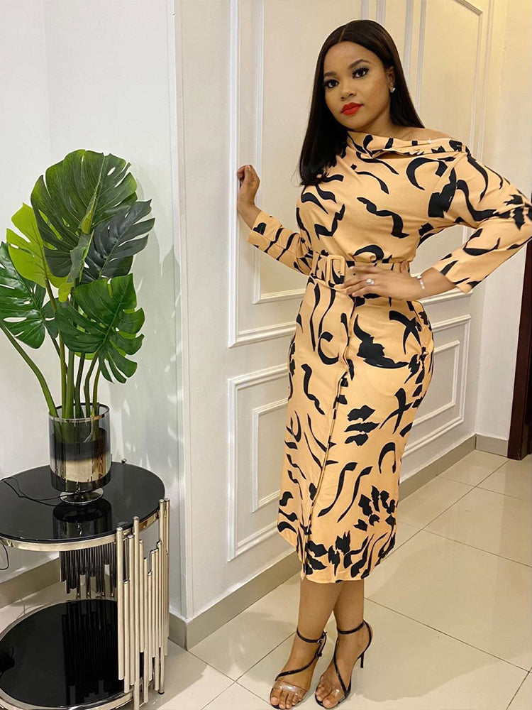 Woman wearing a peach and black abstract print sheath dress with a belted waist and off-the-shoulder neckline.