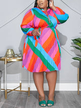 Plus-size woman in a vibrant, long-sleeved, pleated A-line dress with a geometric print and tie-waist, posing with one hand on her head.