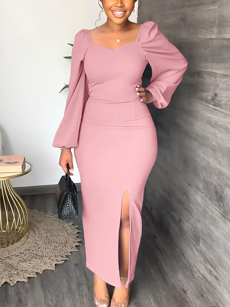 A woman wearing a long pink dress with puff sleeves and a thigh-high slit, holding a black handbag.