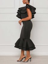 Side view of a woman in a black one-shoulder midi dress with ruffle details and a mermaid hem.