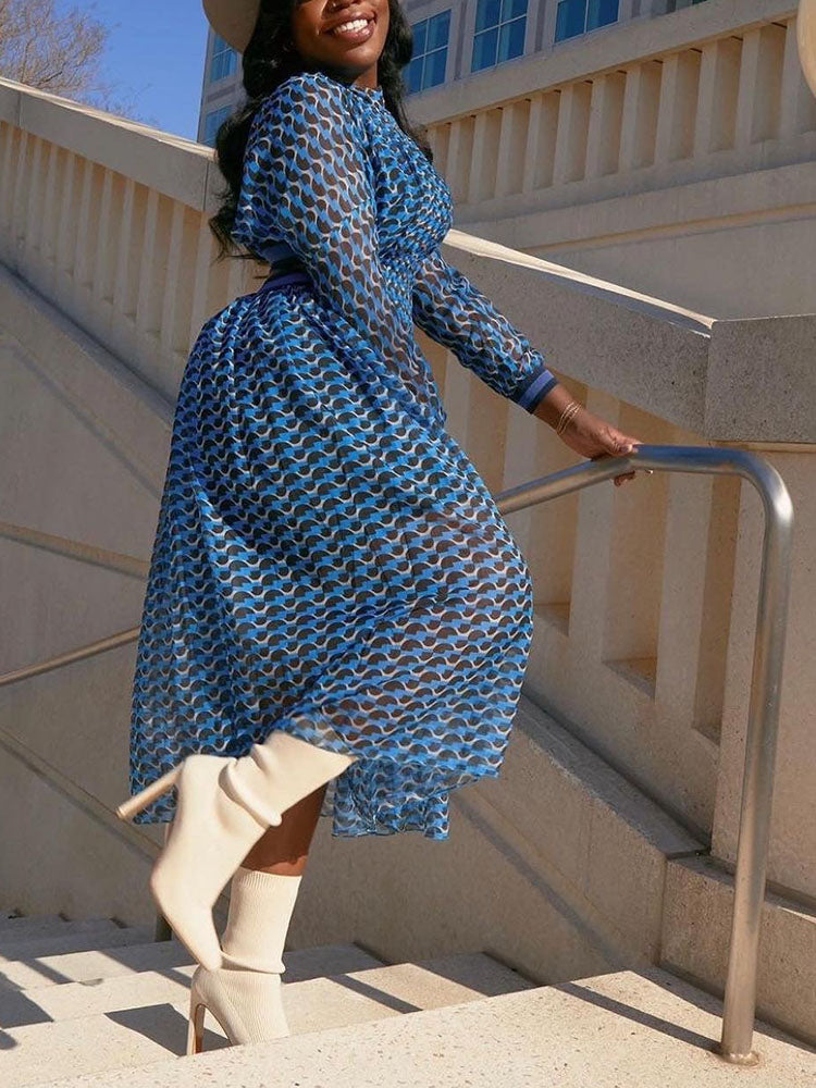 Woman wearing a blue and black geometric print midi dress with cut-out details and long sleeves, walking down stairs in white boots.