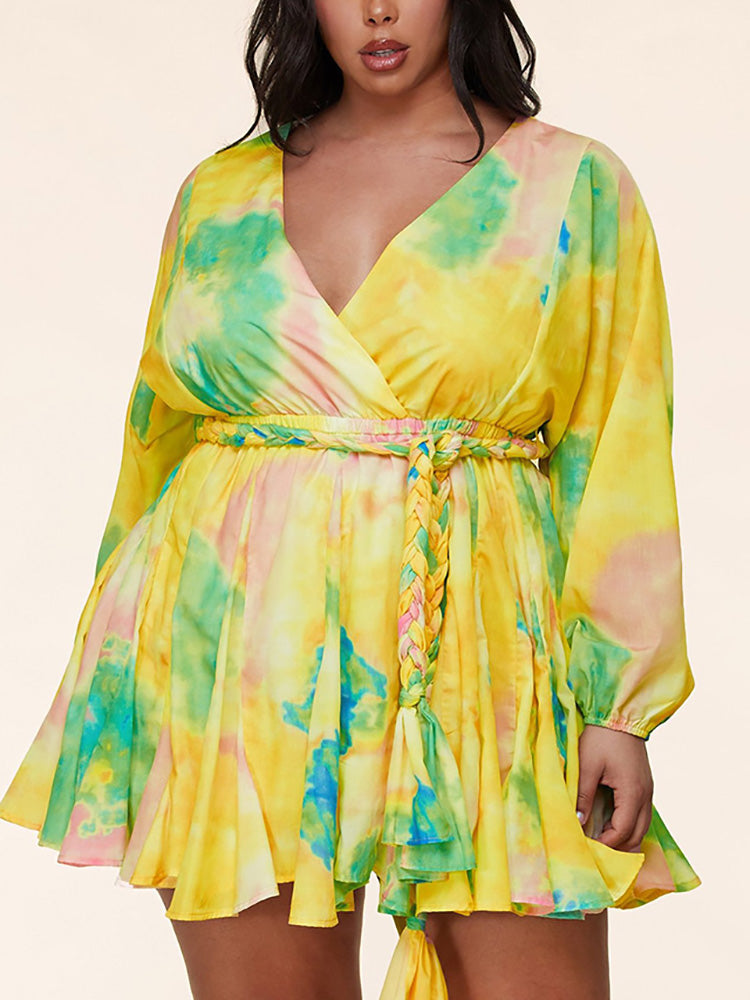 Close-up of a plus-size woman wearing a yellow tie-dye mini dress with a V-neck and belted waist featuring a braided tie.