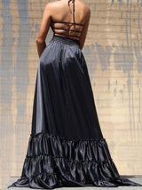 Back view of a woman in a black satin maxi dress with a strappy halter neckline and ruffled hem.