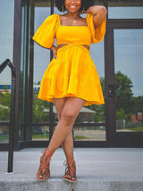 Woman posing in a yellow two-piece set with cut-out details at the waist and a tiered skirt.