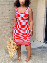 Woman wearing a red and white striped sleeveless dress with a scoop neckline and button detail, holding a straw bag.