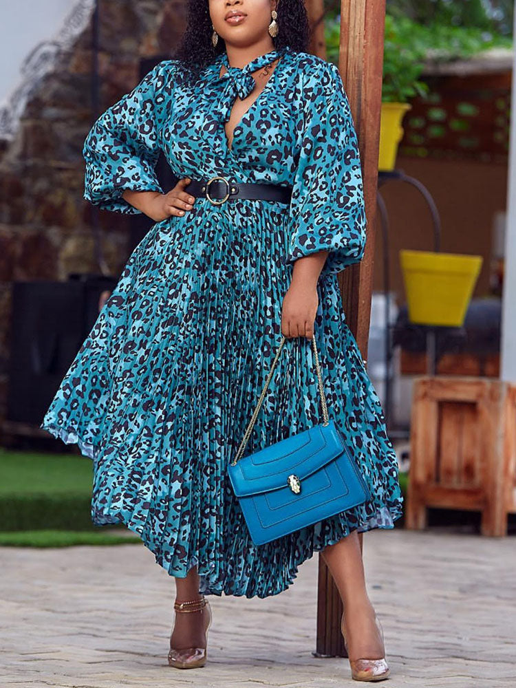 Woman in a blue leopard print midi dress with a bow neckline and pleated skirt, holding a blue handbag and wearing heels.