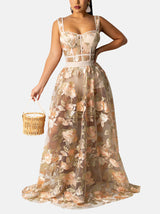 Woman wearing a sheer floral embroidered maxi dress with a corset-style bodice, holding a straw basket.