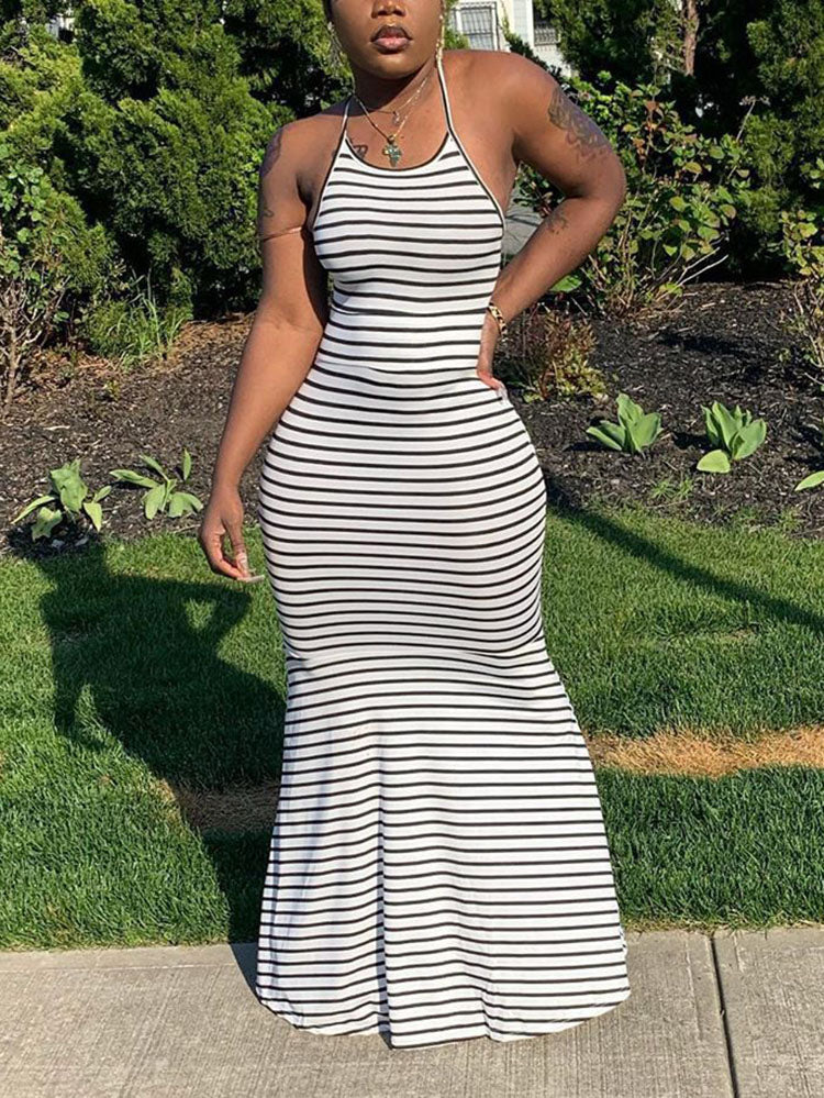 Woman wearing a black and white striped maxi dress with a halter neckline and fishtail hem, standing outdoors.