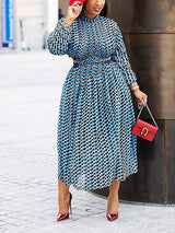 Woman wearing a blue and black geometric print midi dress with cut-out details and long sleeves, paired with red heels and a red handbag.