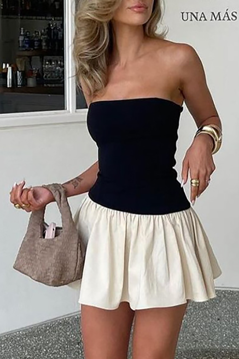 Woman wearing a black strapless top with a cream-colored pleated mini skirt, holding a beige handbag.