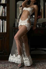 Woman wearing a white sheer lace gown with spaghetti straps and a floor-length skirt, leaning against a bookshelf.