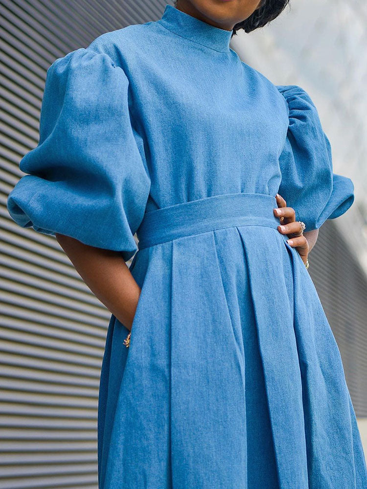 Close-up of a blue denim midi dress with puffed sleeves, high neckline, and belted waist.