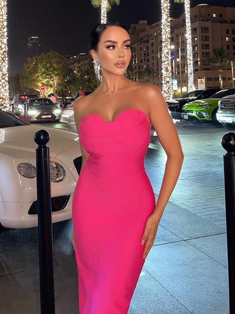 Woman in a bright pink strapless midi dress posing outdoors at night
