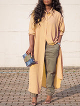 Woman wearing a long yellow collared shirt dress over olive green cargo pants and heels, holding a blue and green clutch.